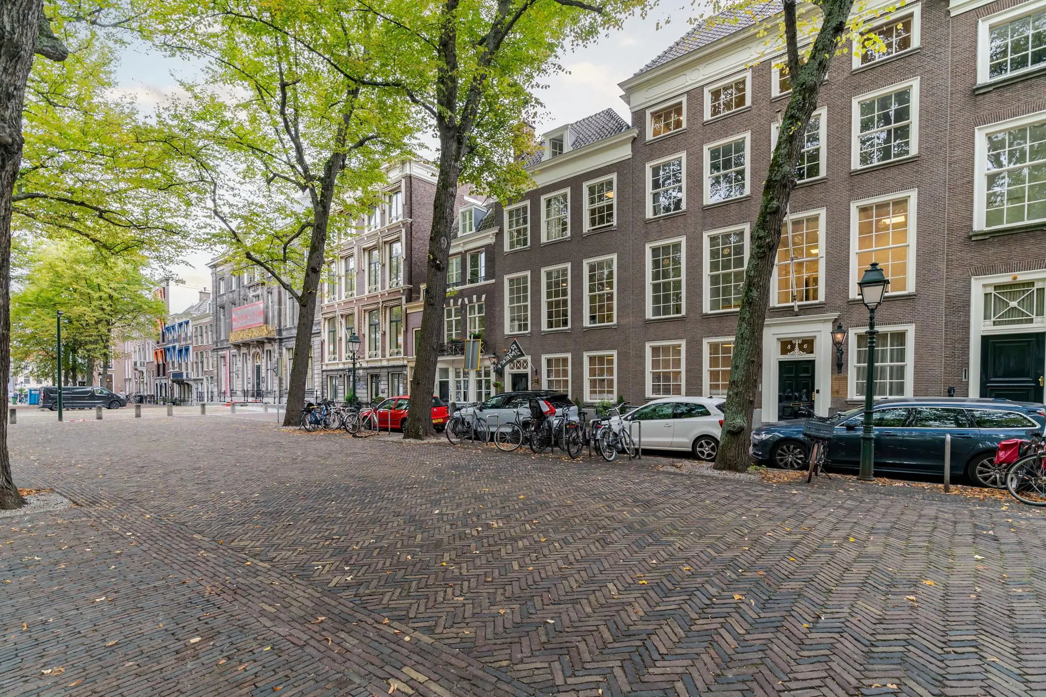 Geplaveide straat met klassieke herenhuizen, fietsen en geparkeerde auto's aan het Lange Voorhout in Den Haag.